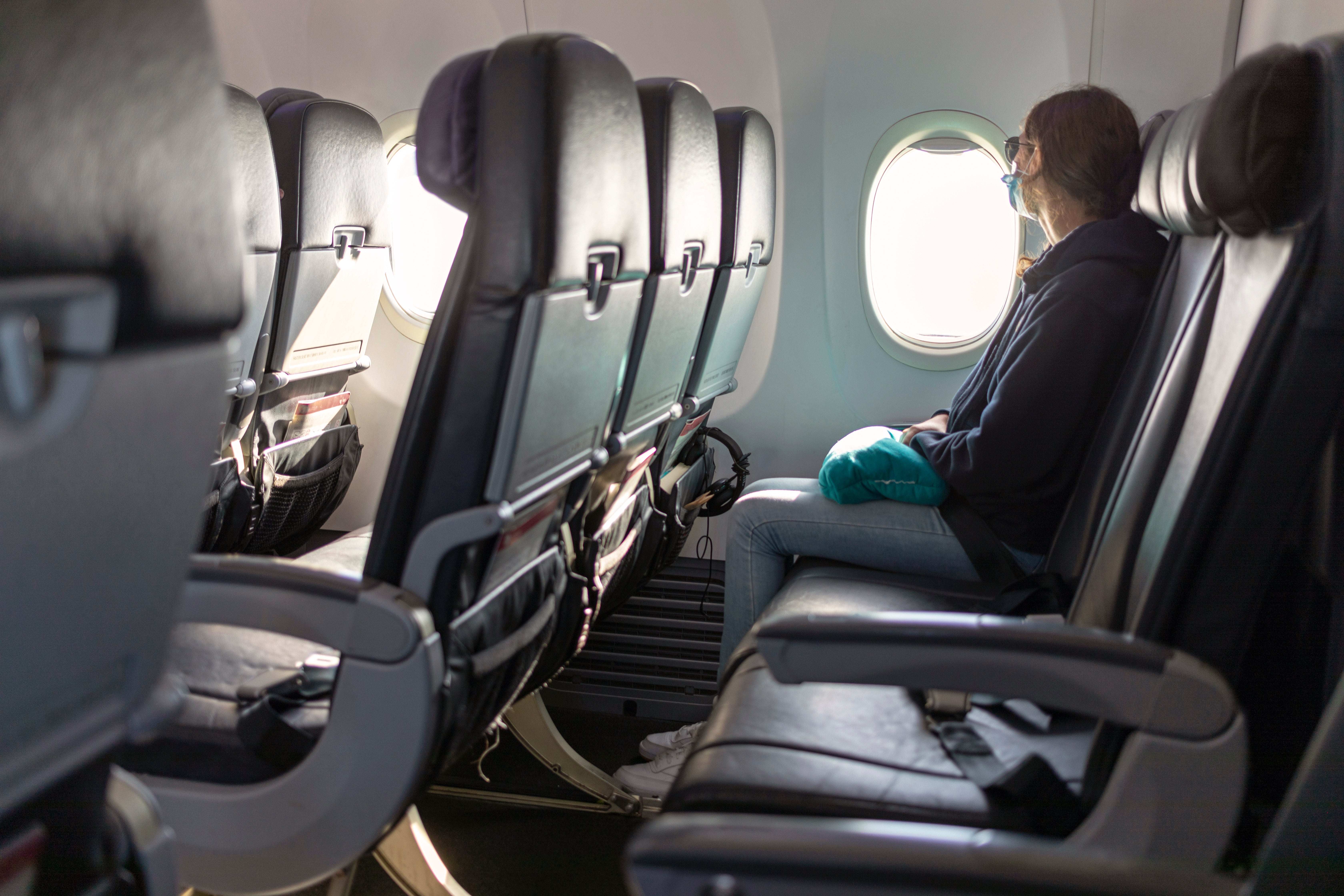Person wearing a mask and gloves sits alone in an airplane, gazing out the window