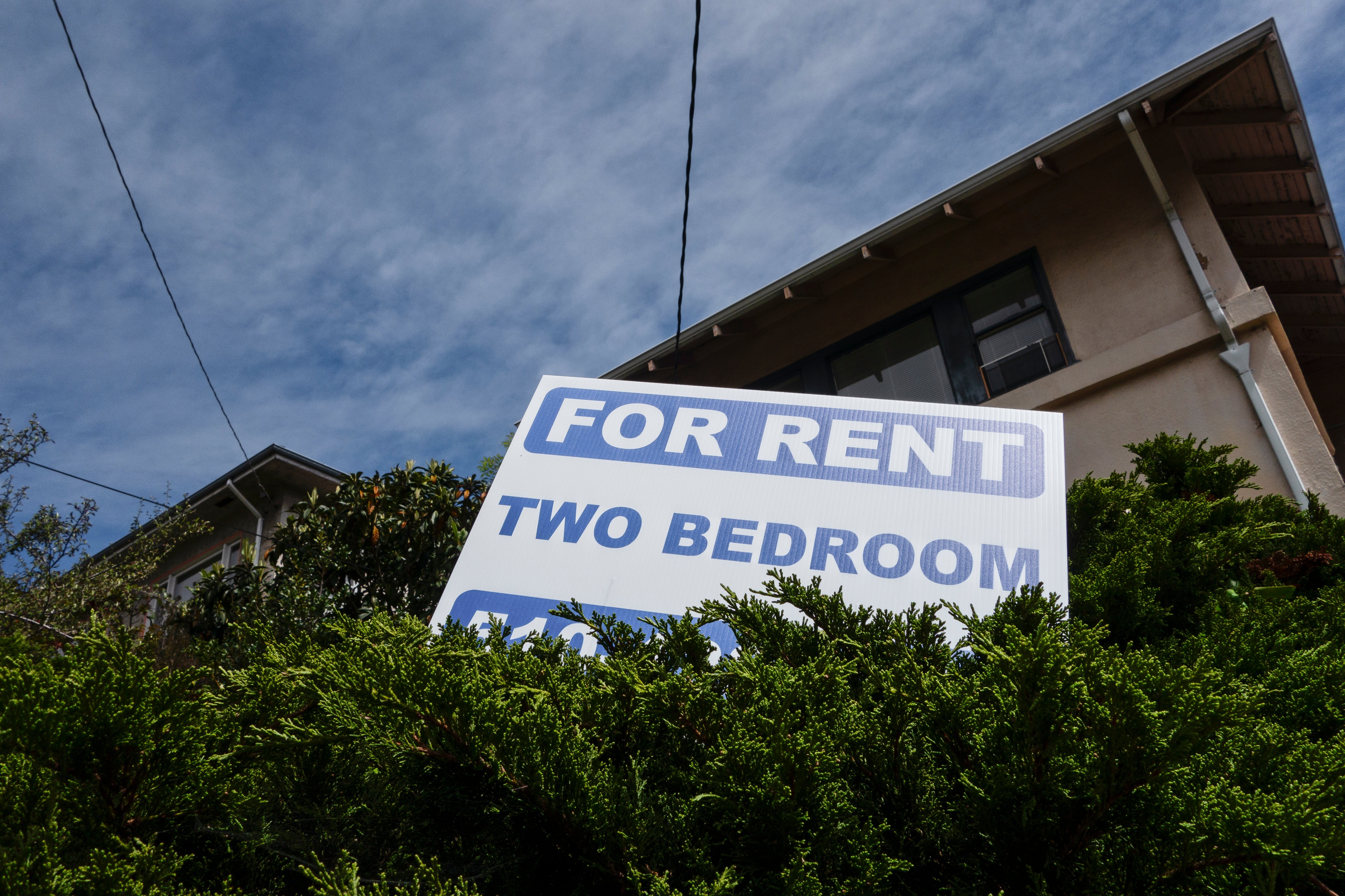 "For Rent" sign for a two-bedroom property in front of a house with leafy surroundings