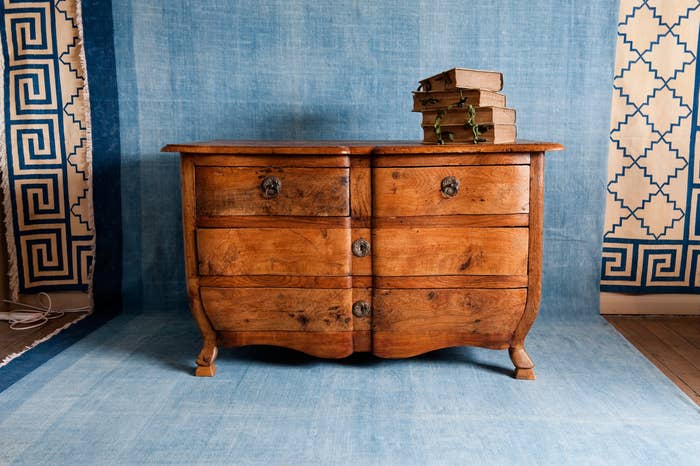 Wooden dresser with antique design and ornate handles, placed on a patterned rug with books stacked on top