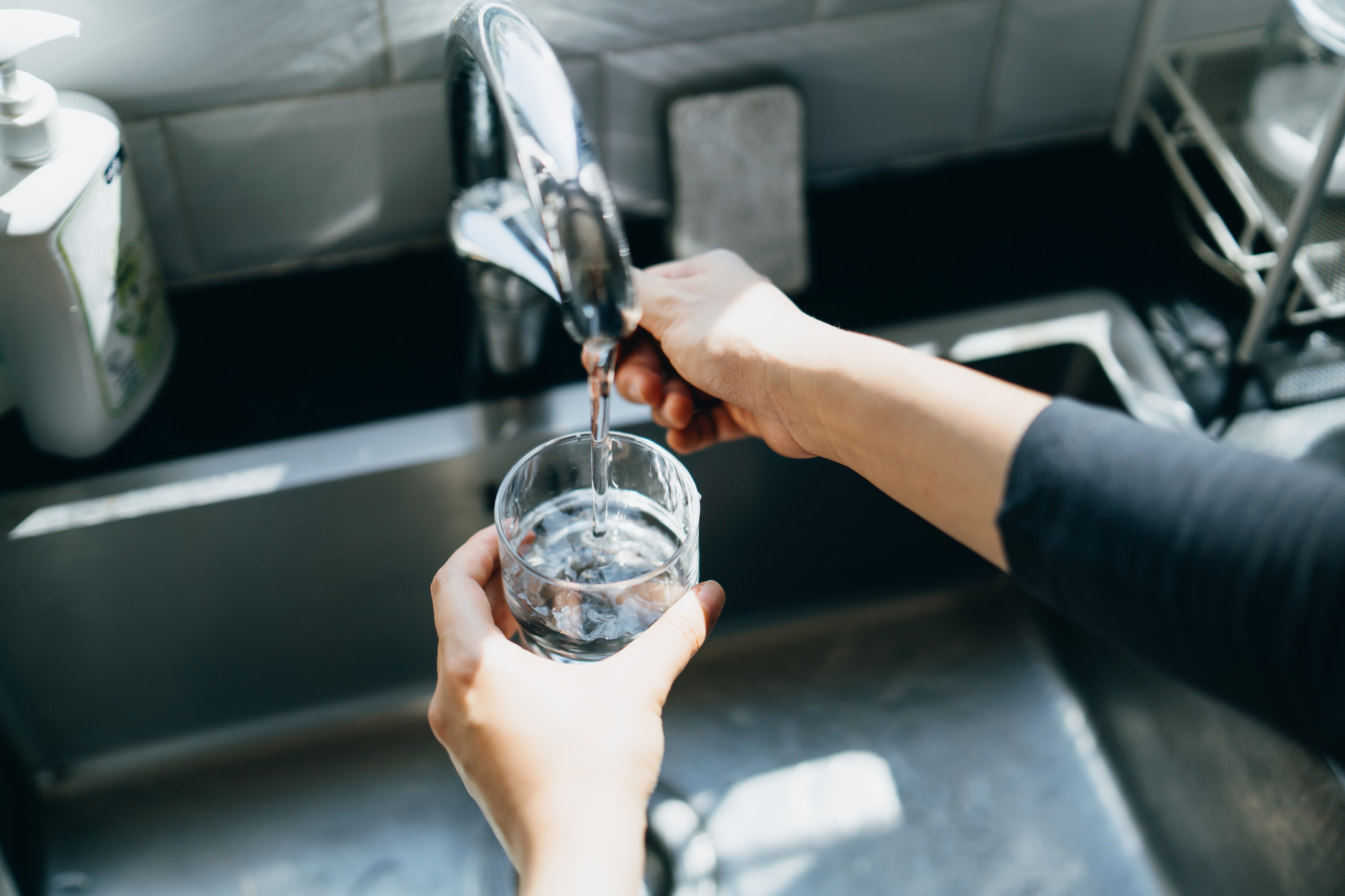 Person filling a glass with water from a kitchen faucet, focusing on clean water access