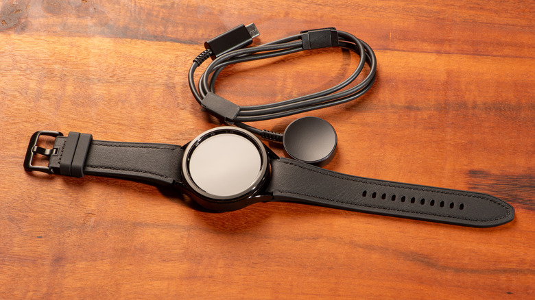 A brown Samsung Galaxy Watch and its charger displayed on a wooden surface.