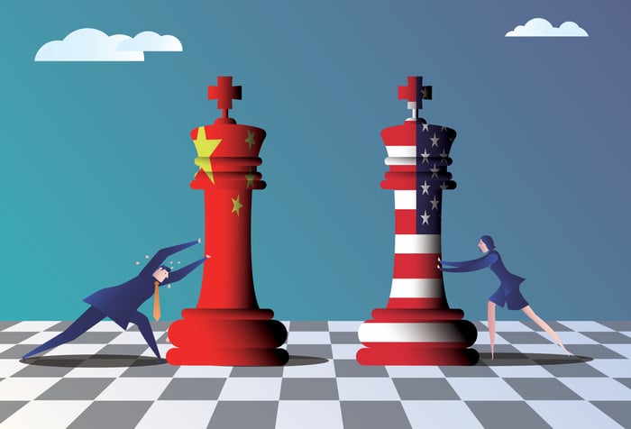 Two cartoon characters pushing giganting chess king toward the middle of a chessboard. One king is emblazoned with the Chinese flag, and the other with the Stars and Stripes.
