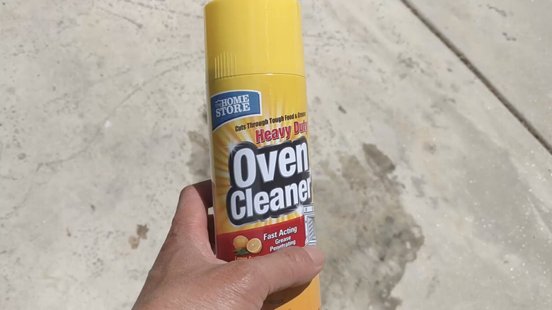 hand holding oven cleaner in front of concrete oil stain
