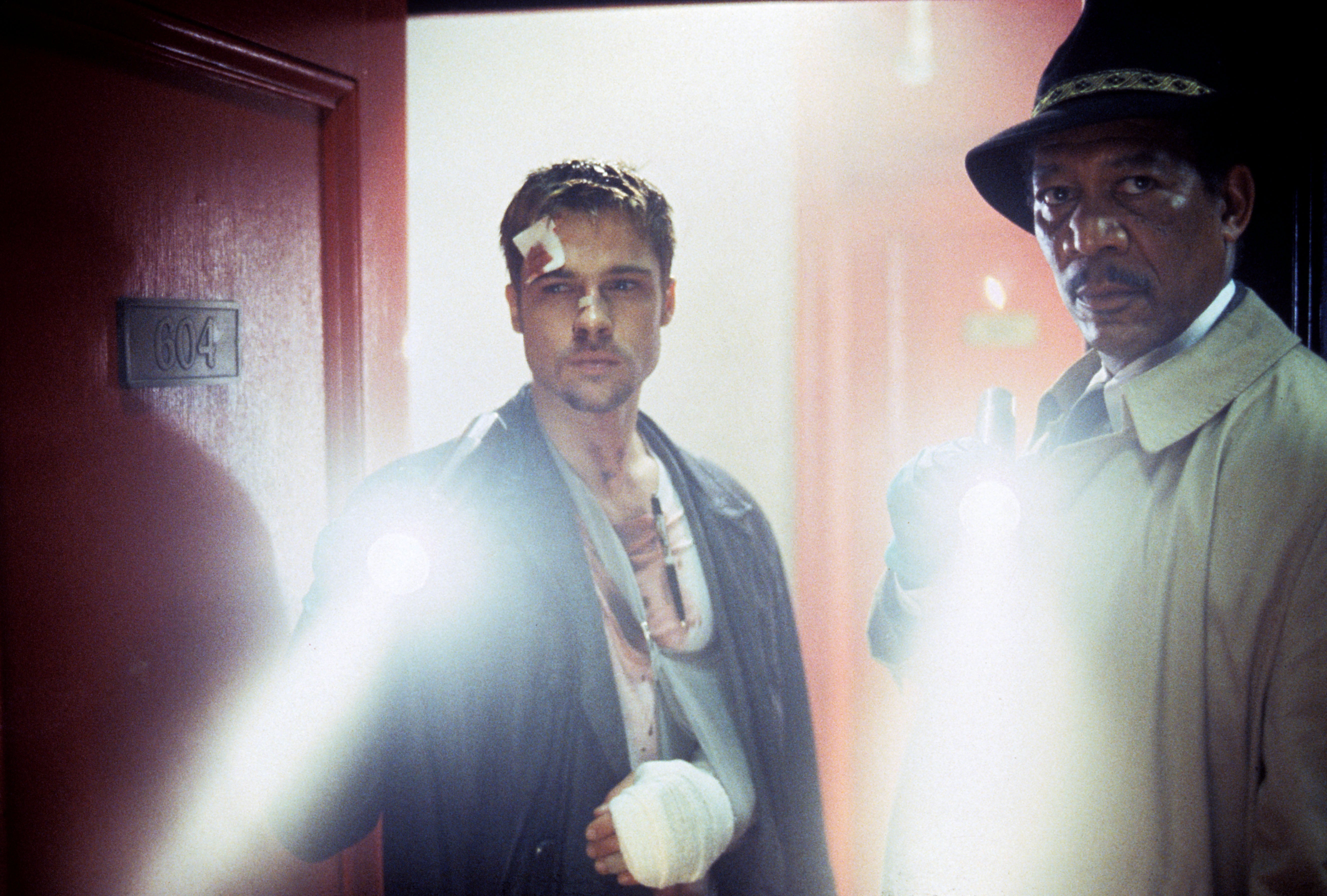 Two detectives, one with a bandaged hand, holding flashlights in a suspenseful scene from a movie