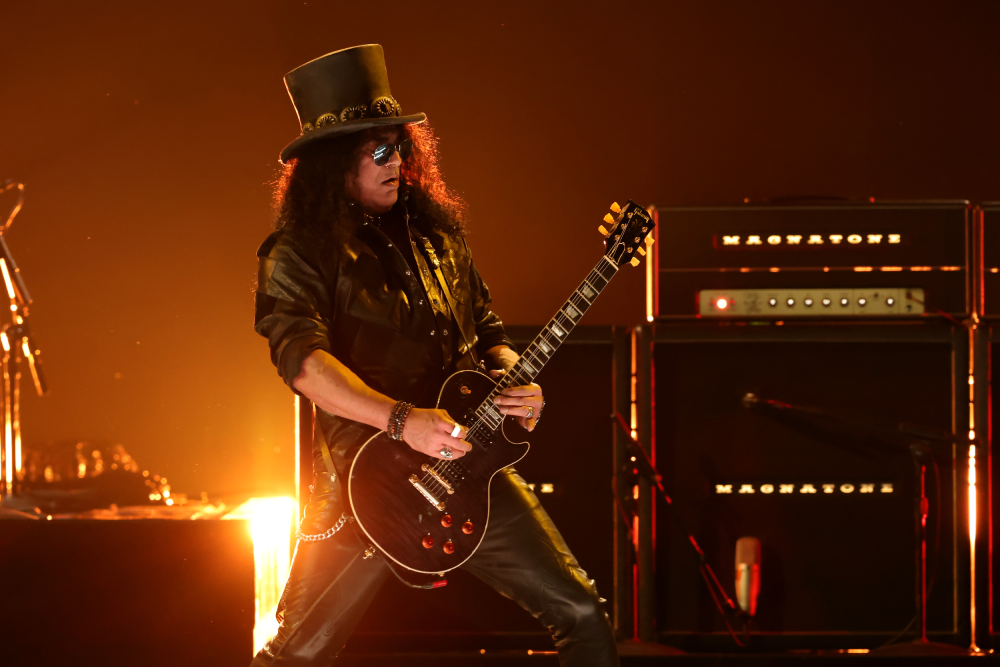 Slash playing an electric guitar on stage in front of Magnatone amplifiers.
