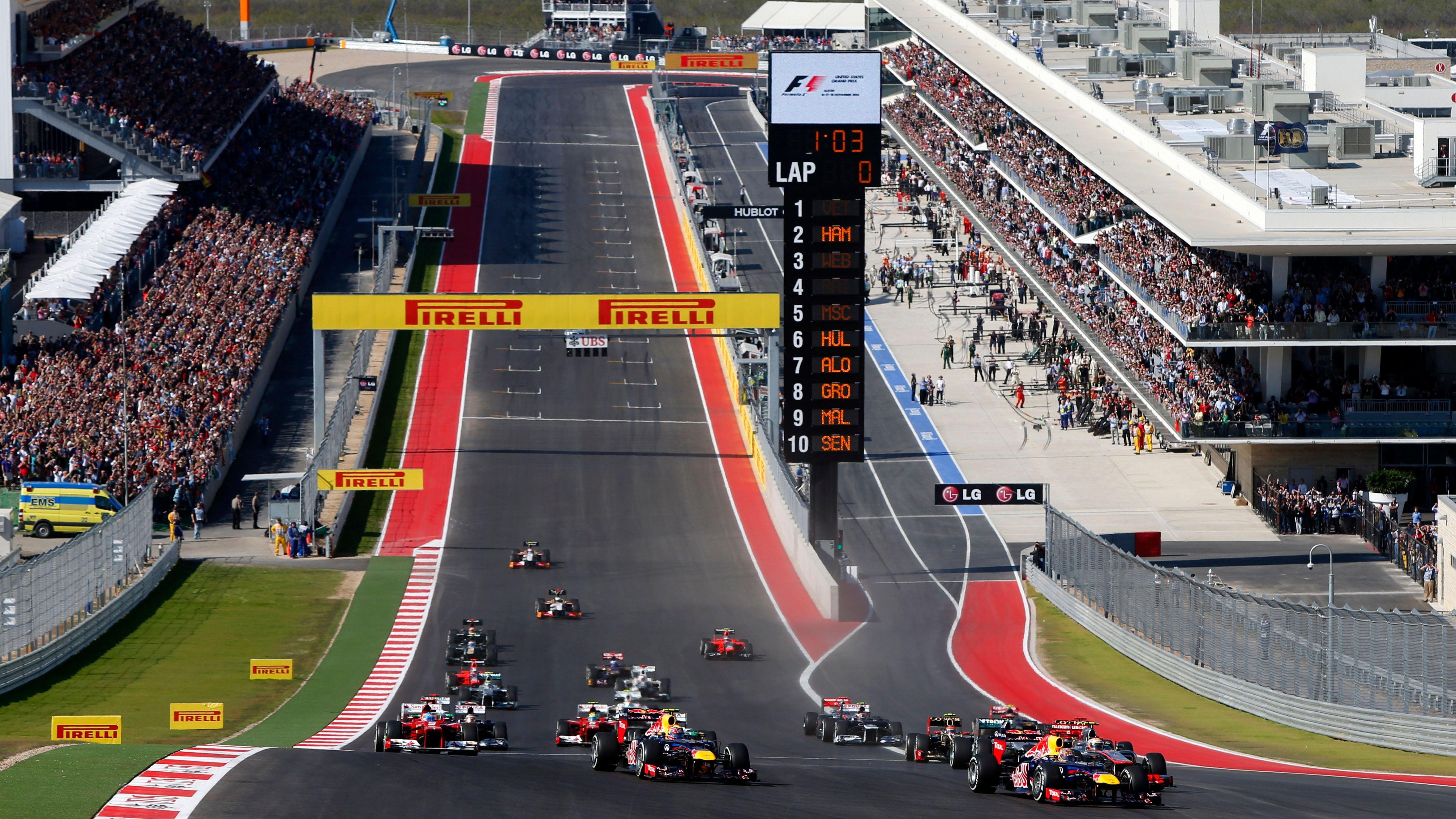 The start of the 2012 US Grand Prix at Austin with the Red Bulls leading the field into the uphill Turn One and a packed grandstand to the left