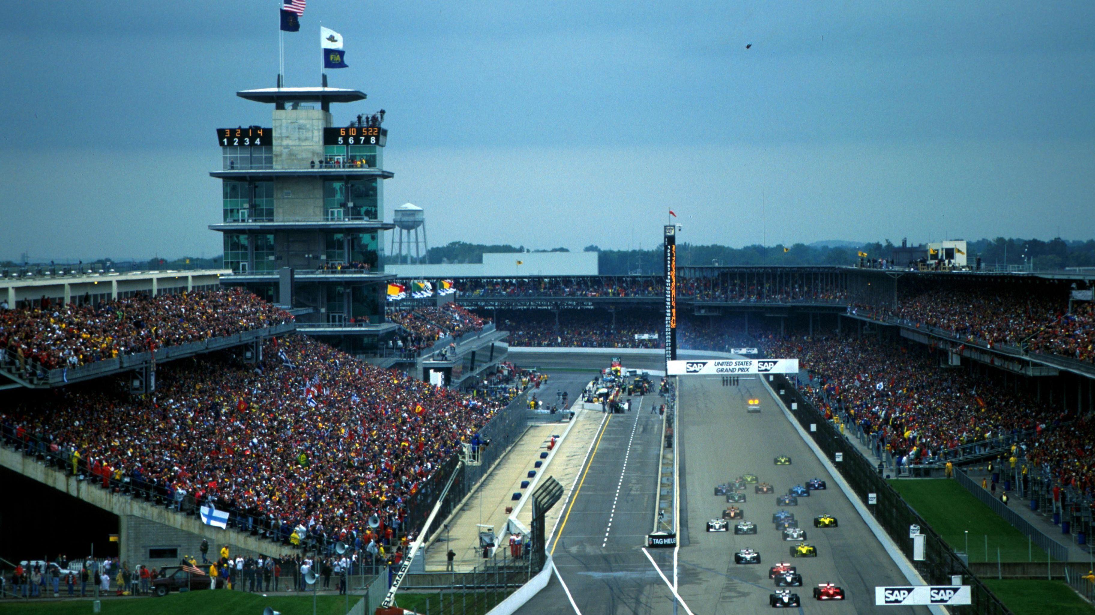 The start of the 2000 US Grand Prix at Indianapolis Motor Speedway with the field racing towards the first turn and packed grandstands surrounding them