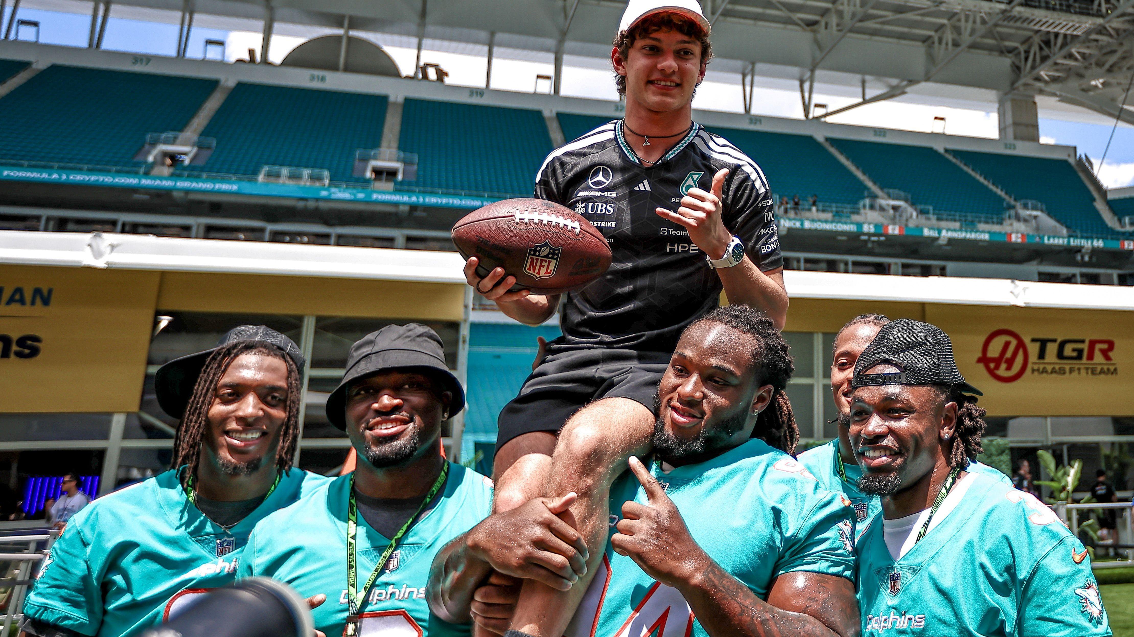 Kimi Antonelli is lifted on to the shoulders of a Miami Dolphins NFL player, while holding an NFL ball, at the Hard Rock Stadium