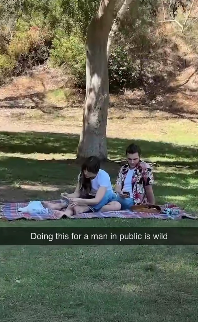 Alison and Dave sitting on a picnic blanket in a park, her clipping his toenails Caption: "Doing this for a man in public is wild"