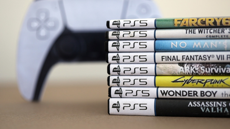 A stack of PS5 game disc boxes with a controller in the background