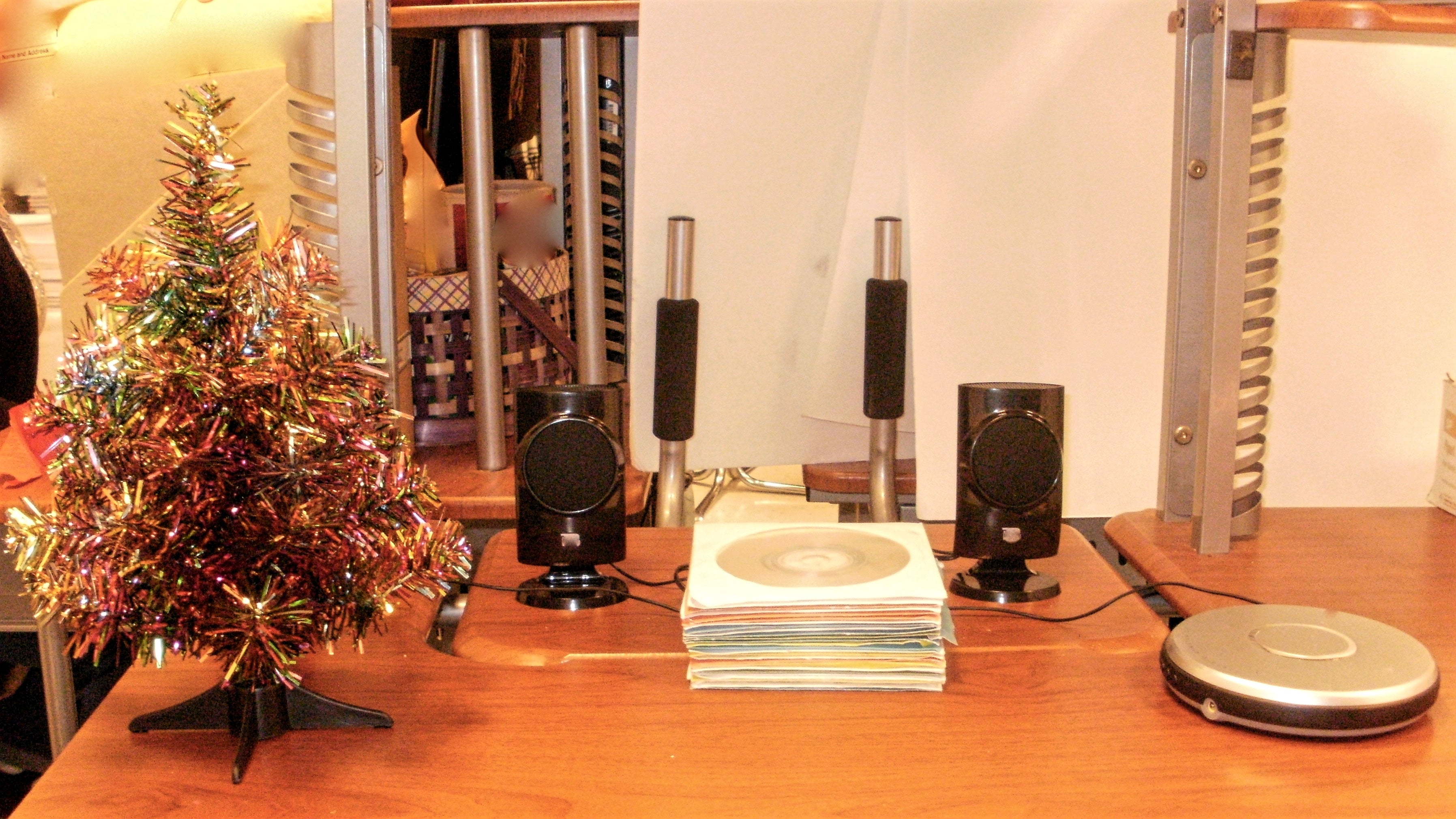A small festive tree next to speakers, a stack of CDs and a portable CD player on a wooden desk